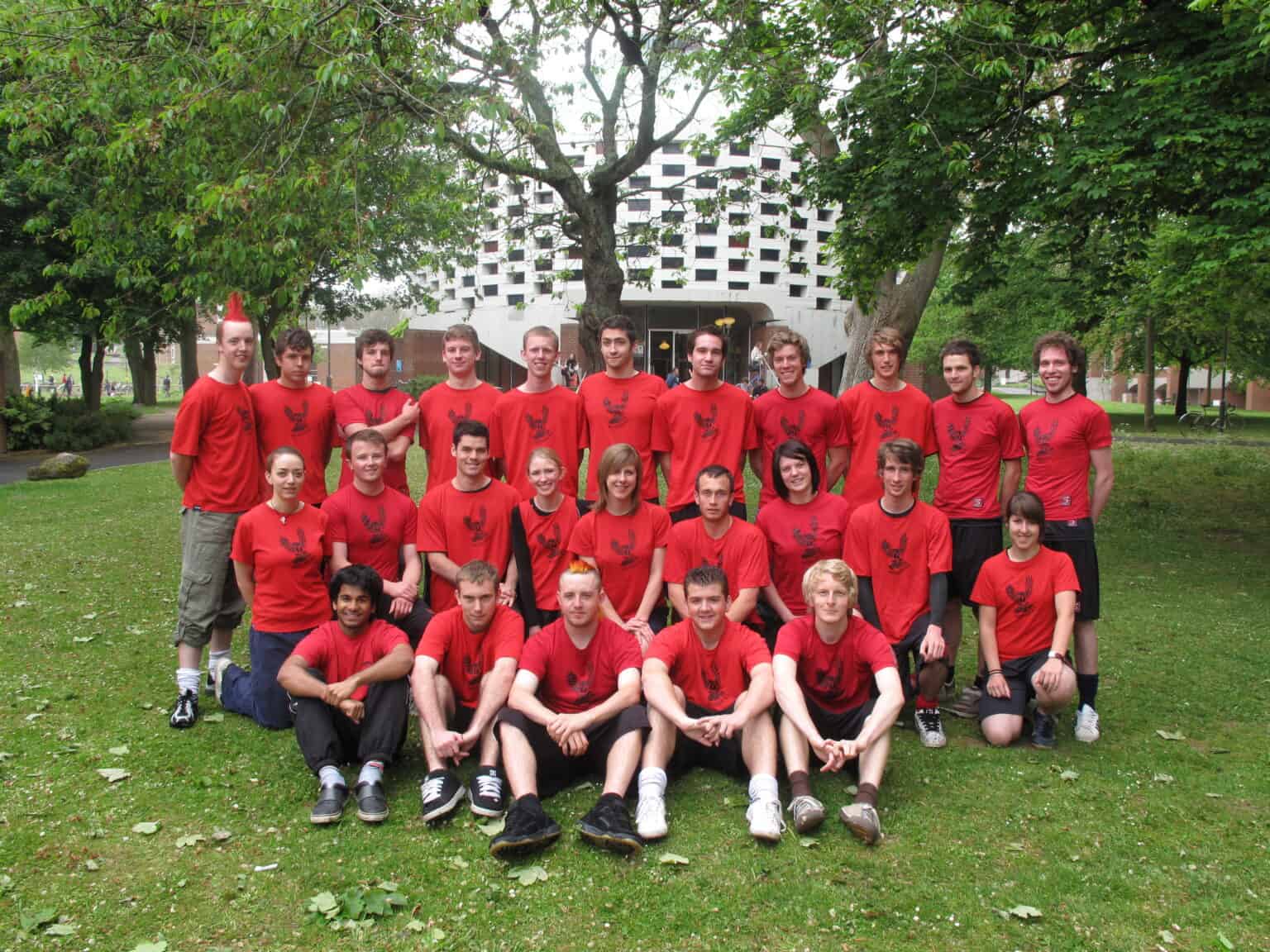 Team of young athletes wearing red shorts and t-shirts with the MoHawks logo, gathered outdoors in a park for a team photo.