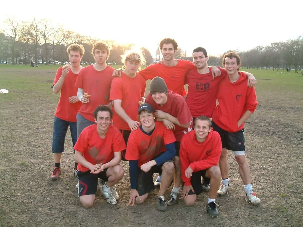 Team of young men celebrating after a game, wearing matching red sports shirts on an outdoor field.