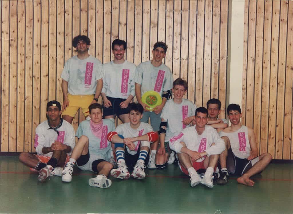 Young men's indoor sports team with Mohawks Ultimate tees, indoor volleyball, gymnasium background, team unity, sports apparel.