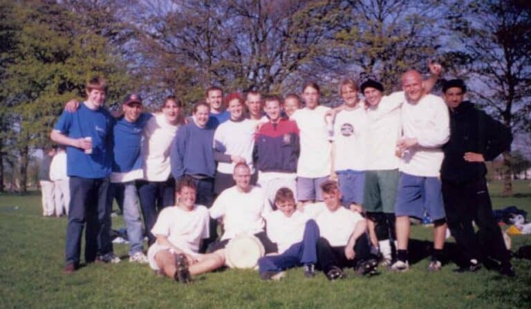 Wide group of young men and boys celebrating outdoors on a sunny day, dressed in sports and casual attire.